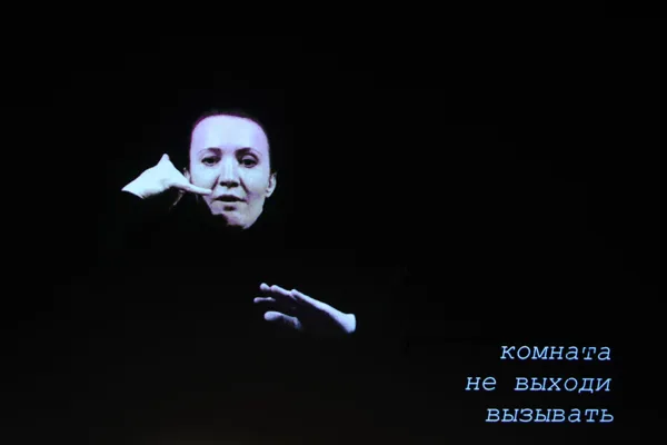 На экране Рахманиновского зала: перформер Юлия Мигунова исполняет в сурдопереводе пьесу Александра Хубеева «Не выходи из комнаты» (2020) для перформера, ансамбля, электроники и видео